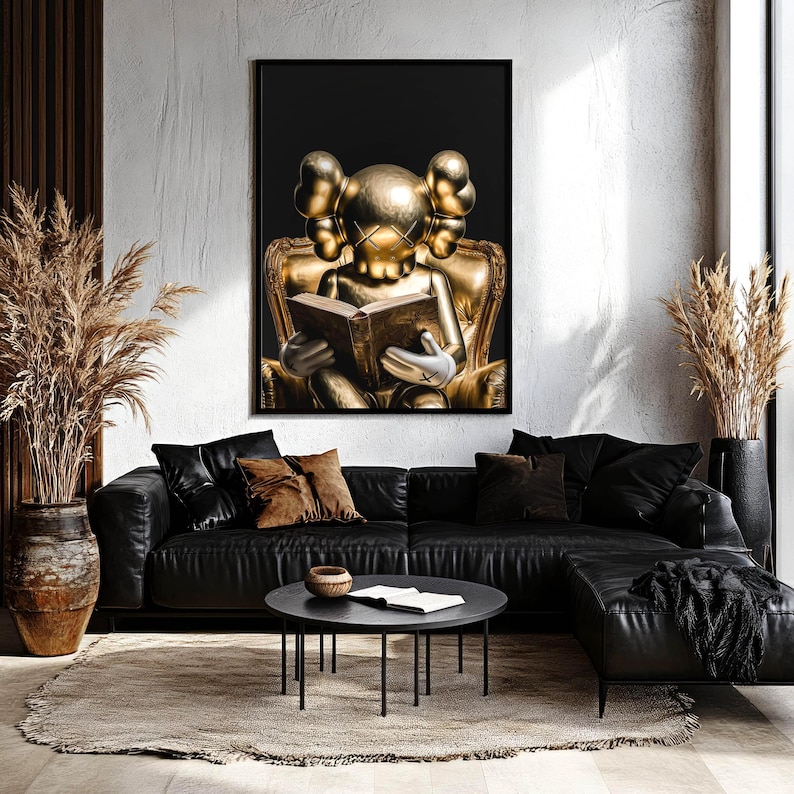 Puede incluir: Una obra de arte enmarcada que presenta una figura dorada leyendo un libro, sobre un fondo negro. La figura est&aacute; sentada en una silla dorada. La habitaci&oacute;n incluye un sof&aacute; seccional de cuero negro, una mesa de centro redonda negra y plantas decorativas.