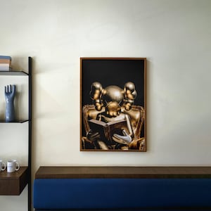 Puede incluir: Una impresi&oacute;n art&iacute;stica enmarcada que presenta una figura dorada leyendo un libro mientras est&aacute; sentada en un sill&oacute;n dorado. La obra de arte tiene un fondo negro y se exhibe en una pared blanca. El marco es de color marr&oacute;n oscuro.