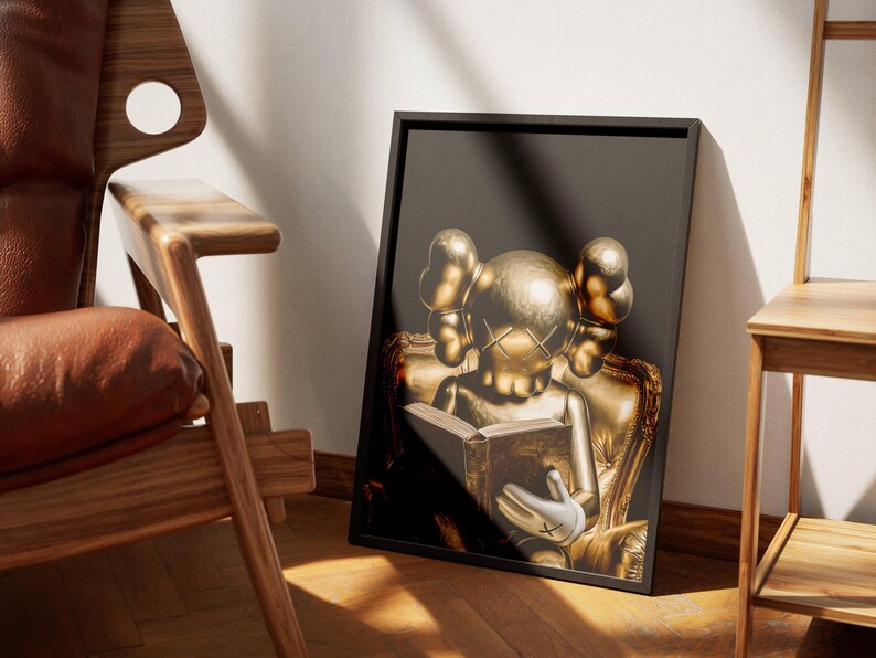 Puede incluir: Una impresi&oacute;n art&iacute;stica enmarcada que presenta una figura dorada leyendo un libro, sobre un fondo oscuro. La figura est&aacute; sentada en una silla dorada. La obra de arte se muestra en un marco negro, apoyada contra una pared cerca de una silla de madera.