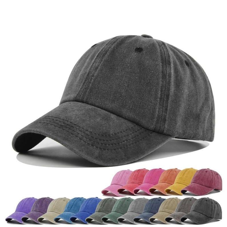 May include: A dark gray baseball cap with a curved brim. The cap is made of a soft, textured fabric. Below, a row of baseball caps in various colors, including purple, blue, green, and pink, are displayed.