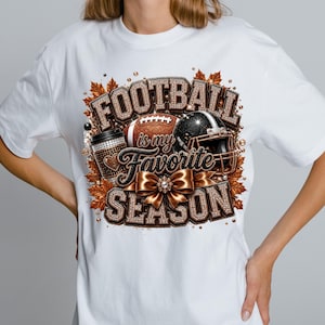 Puede incluir: Una camiseta blanca con un dise&ntilde;o gr&aacute;fico que incluye el texto "FOOTBALL is my Favorite SEASON". El dise&ntilde;o presenta un bal&oacute;n de f&uacute;tbol americano marr&oacute;n, un casco negro, una taza de caf&eacute; y un lazo de color bronce met&aacute;lico, rodeado de hojas.