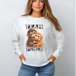 May include: White long-sleeve sweatshirt with the text "TEAM PUNCH" above and below an illustration of two hugging monkeys. The monkeys are brown and orange with large eyes. The sweatshirt is worn by a person.