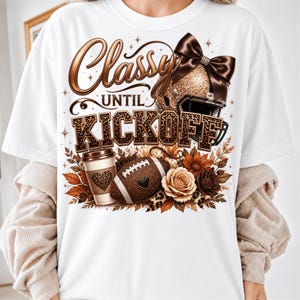 Puede incluir: Una camiseta blanca con un gr&aacute;fico que incluye el texto Classy UNTIL KICKOFF. El dise&ntilde;o muestra un casco de f&uacute;tbol americano brillante con un lazo marr&oacute;n, un vaso de caf&eacute; con un coraz&oacute;n de leopardo, un bal&oacute;n de f&uacute;tbol y flores marrones y crema.
