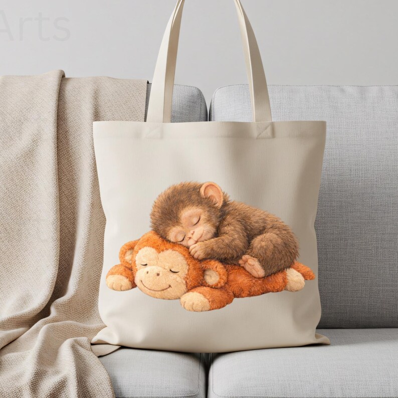 May include: A beige tote bag featuring a watercolor illustration of two sleeping monkeys. One small, brown monkey is nestled on top of a larger, orange monkey. The bag has long handles and is made of a canvas-like material.