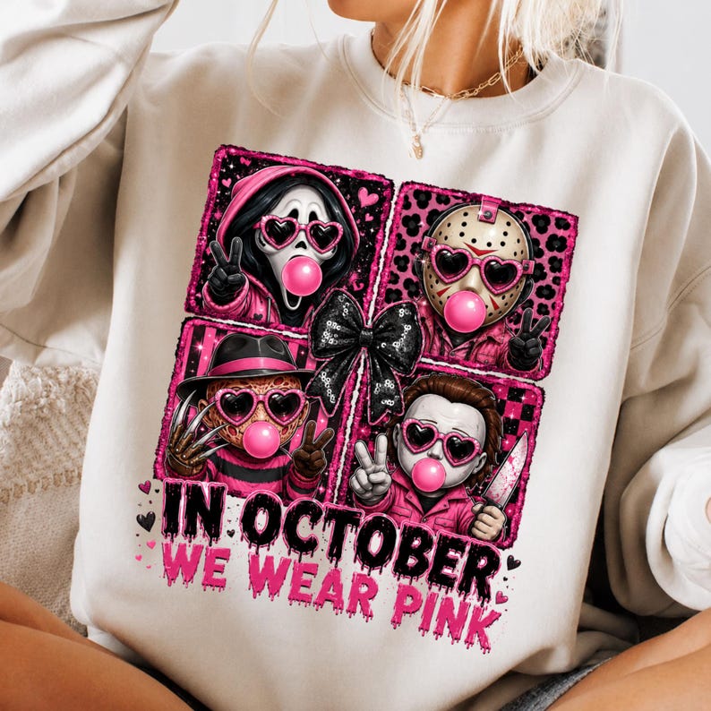 May include: A cream-colored sweatshirt featuring a graphic print of four horror movie characters wearing pink heart-shaped sunglasses and blowing pink bubblegum bubbles. A black bow sits in the center. The text reads, IN OCTOBER WE WEAR PINK.