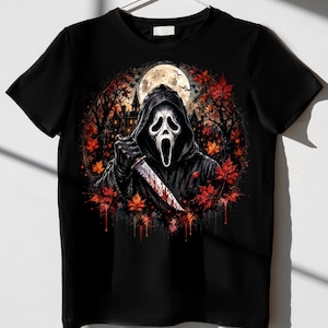 May include: A black short-sleeve t-shirt featuring a graphic print of a hooded figure in a white mask holding a bloody knife. The design includes a full moon, a dark silhouette of a house, and vibrant red and orange autumn maple leaves.