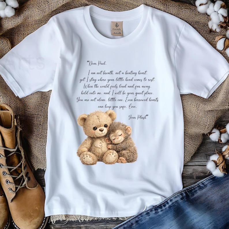 May include: White t-shirt featuring a watercolor illustration of a teddy bear and a monkey hugging. The shirt includes a poem about comfort and love. The text reads "Dear Puck" and "Your Plush".