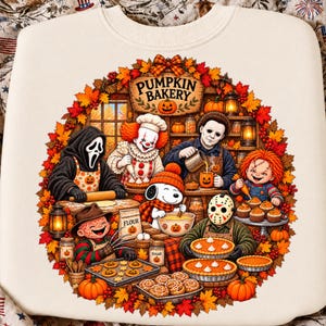 Pode incluir: Uma camisola cor de creme com um gráfico circular de várias personagens de filmes de terror e um cão de desenho animado a cozinhar numa cozinha com a etiqueta PUMPKIN BAKERY. A cena inclui folhas de outono, abóboras, tartes e utensílios.