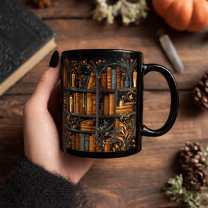 Puede incluir: Taza de cer&aacute;mica negra con una ilustraci&oacute;n detallada de una estanter&iacute;a llena de libros, velas y elementos bot&aacute;nicos. El dise&ntilde;o incorpora tonos dorados, marrones y azules sobre un fondo negro. La taza tiene un asa negra.
