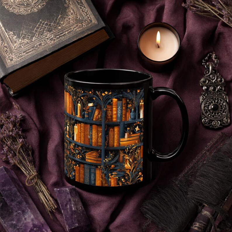 Puede incluir: Taza de cer&aacute;mica negra con una ilustraci&oacute;n detallada de una estanter&iacute;a llena de libros y velas. El dise&ntilde;o incluye tonos naranja, azul y dorado. Tambi&eacute;n se ven una vela encendida, un colgante decorativo y un libro antiguo.