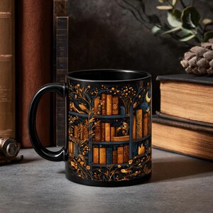 Puede incluir: Taza de cer&aacute;mica negra con una ilustraci&oacute;n detallada de una estanter&iacute;a llena de libros. El dise&ntilde;o incluye detalles dorados y azules, con una luna creciente y elementos florales. La taza tiene un asa negra y un acabado brillante.