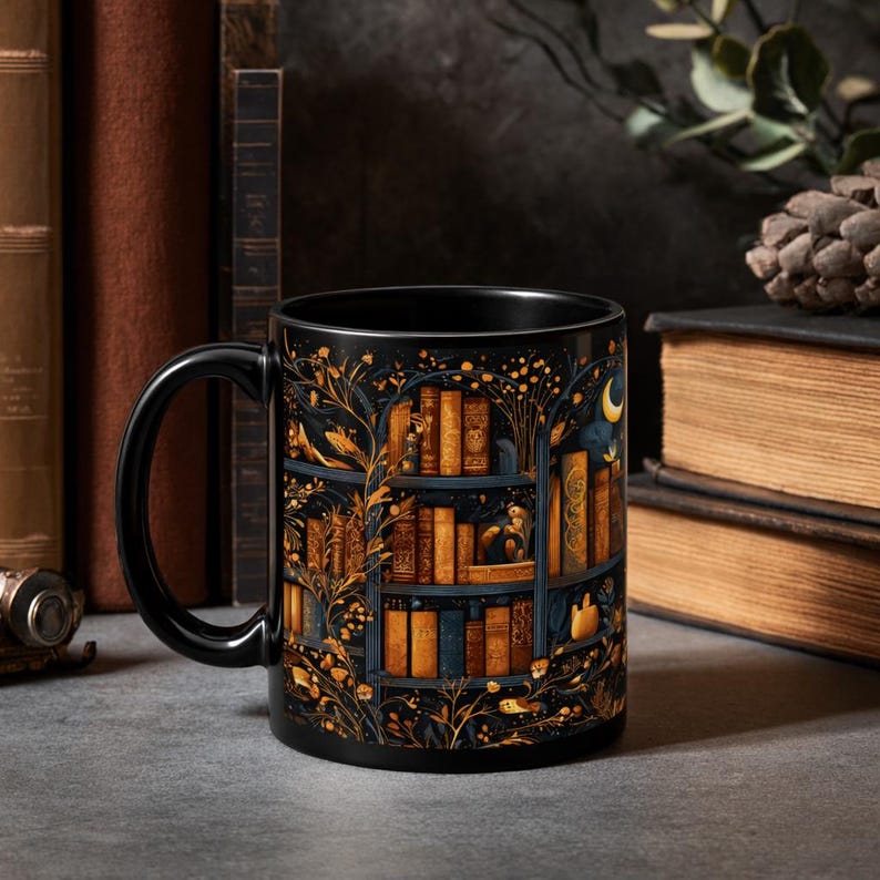 Puede incluir: Taza de cer&aacute;mica negra con una ilustraci&oacute;n detallada de una estanter&iacute;a llena de libros. El dise&ntilde;o incluye detalles dorados y azules, con una luna creciente y elementos florales. La taza tiene un asa negra y un acabado brillante.