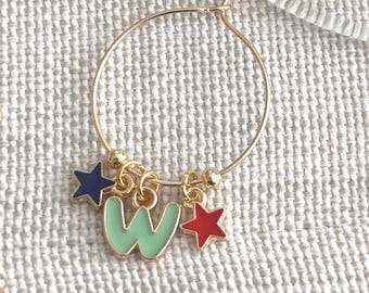 May include: Gold hoop earring with a mint green letter "W" charm, a navy blue star, and a red star. The charms are enamel-filled and hang from the gold hoop. The earring is a fun and colorful accessory.