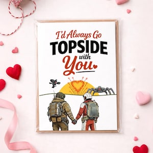 May include: Greeting card with the text "I'd Always Go TOPSIDE with You." The card features two figures in space suits holding hands, with a sunset and space-themed illustrations. Hearts and ribbons surround the card.