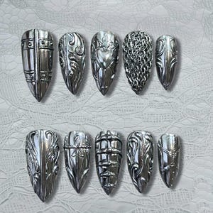 Può includere: Un set di dieci unghie finte color argento. Ogni unghia presenta un design unico, tra cui volute ornate, cotta di maglia e un cuore. Le unghie a forma di mandorla hanno una finitura metallica.