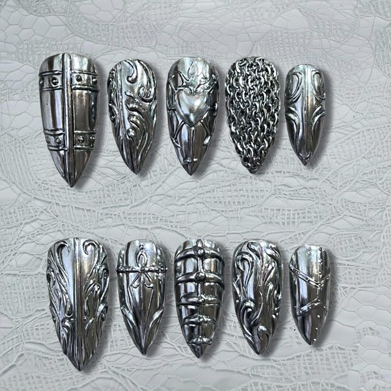 Puede incluir: Un conjunto de diez u&ntilde;as postizas plateadas. Cada u&ntilde;a presenta un dise&ntilde;o &uacute;nico, que incluye adornos ornamentados, cota de malla y un coraz&oacute;n. Las u&ntilde;as en forma de almendra tienen un acabado met&aacute;lico.