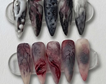 May include: A set of ten long, pointed false nails with a Halloween theme. The nails feature a variety of designs, including white, black, and red colour schemes, with textures and patterns that resemble gore, decay, and abstract art.