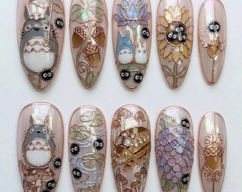 Könnte beinhalten: Ein Set aus zehn mandelförmigen Nageldesigns. Jeder Nagel zeigt ein anderes Design, darunter Totoro-Charaktere, Eicheln, eine Sonnenblume und einen Bus, alles im detaillierten Cartoon-Stil mit Perlmutt-Finish.