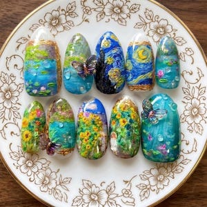 May include: A set of ten press-on nails featuring intricate, textured art inspired by famous paintings, including swirling blue night skies, vibrant yellow sunflowers, and water lily ponds, accented with small, translucent 3D butterfly charms.