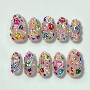 May include: A set of ten artificial nails, each painted a pale pink and adorned with colorful, sparkling embellishments. The decorations include various shapes like hearts, stars, and flowers, in shades of red, blue, green, and gold. The nails are arranged on a white surface.