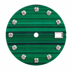Peut inclure: Un cadran de montre circulaire présentant une surface en pierre de malachite verte vibrante avec des bandes horizontales. Le cadran comprend dix index carrés argentés sertis de petites pierres claires et un guichet de date rectangulaire.