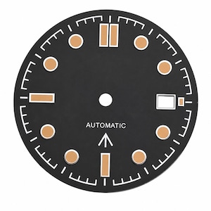 Op de afbeelding: Een ronde zwarte wijzerplaat met witte minuutmarkeringen, beige ronde en rechthoekige uurindexen en een wit datumvenster op de drie-uurpositie. Het woord AUTOMATIC is in het wit gedrukt boven een witte pijl die naar boven wijst.