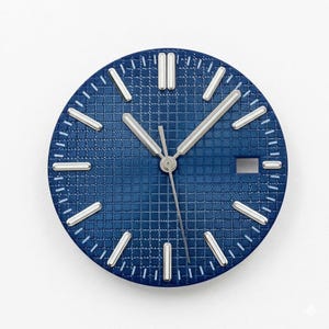 Könnte beinhalten: Blaues Zifferblatt mit strukturiertem Gittermuster. Silberfarbene Zeiger und Stundenmarkierungen. Das Zifferblatt hat ein Datumsfenster bei 3 Uhr. Das Design ist modern und minimalistisch.