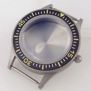 Puede incluir: Una caja de reloj de acero inoxidable plateado con un bisel giratorio negro que presenta números amarillos en el 15, 30 y 45, junto con marcas amarillas. La caja incluye un cristal circular, una corona lateral y dos pasadores.