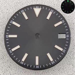 May include: A round black watch dial featuring white minute markers in increments of five, rectangular hour indices, and a triangular marker at the twelve o'clock position. A rectangular date window is located at the three o'clock position.