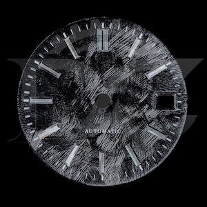 Può includere: Un quadrante per orologio rotondo nero con una finitura spazzolata e testurizzata, dotato di indici rettangolari color argento. Il quadrante presenta una finestrella per la data a ore tre e la scritta AUTOMATIC stampata in bianco al centro.