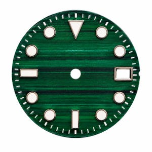 Può includere: Un quadrante circolare per orologio caratterizzato da un motivo verde intenso simile alla malachite con bande orizzontali. Include indici applicati color argento con centri bianchi luminescenti, tra cui un triangolo a ore dodici e rettangoli a tre, sei e nove.