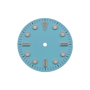 May include: A circular watch dial in a matte light blue finish featuring a central hole, black minute track markers, and raised silver-toned indices. The indices include circular dots, rectangular bars at three, six, and nine, and a triangular marker at twelve.