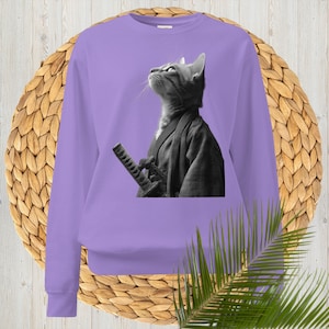 Może przedstawiać: Liliowa bluza z czarno-białym wizerunkiem kota ubranego w strój samuraja, z kataną. Kot patrzy w górę. Bluza ma długie rękawy i okrągły dekolt.