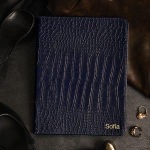 May include: A rectangular dark blue notebook with a textured crocodile skin pattern. The name Sofia is embossed in gold lettering in the bottom right corner. The notebook is positioned centrally, featuring stitched edges and a structured, firm cover.