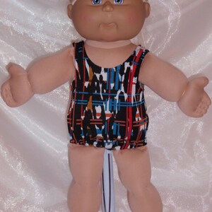 May include: A Cabbage Patch Kid doll wearing a black, blue, and orange swimsuit with a geometric pattern.