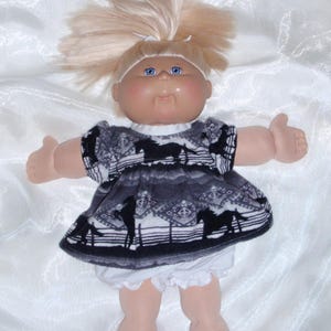 May include: A vintage doll with blonde hair styled in a high ponytail. The doll has blue eyes and rosy cheeks. It is wearing a black and white patterned dress with a horse design and white ruffled bloomers.