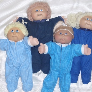 May include: Four Cabbage Patch Kids dolls wearing blue pajamas. The dolls have blonde hair and blue eyes.