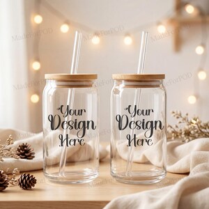 Puede incluir: Dos vasos transparentes para bebidas con tapas de bambú y pajitas transparentes. Las tazas tienen el texto "Your Design Here" en escritura negra. El fondo incluye luces de hadas y elementos decorativos.