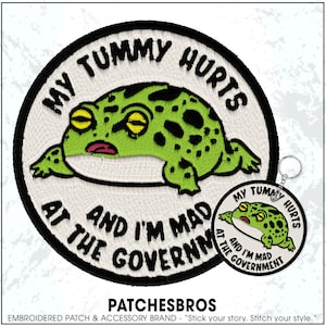 May include: Embroidered patch and keychain set featuring a green frog with black spots. The patch and keychain have the text "MY TUMMY HURTS AND I'M MAD AT THE GOVERNMENT" in a circular design. The brand name "PATCHESBROS" is at the bottom.