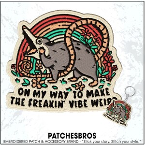 May include: Embroidered patch featuring a cartoon opossum with a rainbow and floral accents. Text reads "ON MY WAY TO MAKE THE FREAKIN VIBE WEIRD." A matching keychain is also visible. The patch is from the PatchesBros brand.