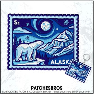 May include: Embroidered patch featuring a polar bear in a snowy Alaskan landscape under a starry night sky. The design includes mountains, a full moon, and the word "ALASKA". A matching keychain is also visible.