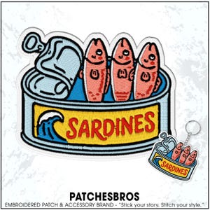 May include: Embroidered patch featuring a cartoon sardine can with three pink fish. The can is blue and yellow with the word "SARDINES" in red. A small keychain with a similar design is also visible.