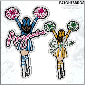 May include: Embroidered patches featuring cheerleader designs. One patch is blue and white with the name "Anyname", and the other is yellow and white with the name "Sophia". Both patches have pom-poms and are outlined in black.