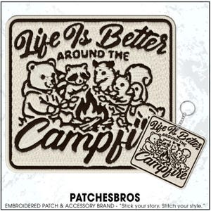 May include: Embroidered patch with the text "Life Is Better Around The Campfire" and a graphic of woodland creatures around a campfire. A matching keychain is also shown. The patch is beige with brown embroidery.