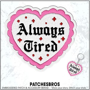 May include: A heart-shaped embroidered patch with the words "Always Tired" in black gothic lettering. The patch has a white center, a pink scalloped border, and red diamond and dot accents. A matching keychain is also visible.