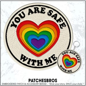 May include: Embroidered patch and keychain set featuring a rainbow heart design. The patch and keychain have the text "YOU ARE SAFE WITH ME" in a circular design. The patch and keychain are cream-colored with black text and a black border.