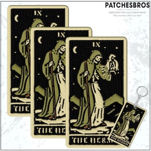 May include: Embroidered patches and a keychain featuring the Hermit tarot card design. The patches and keychain have a black background with a figure in a green robe, a staff, and a crescent moon. The text "THE HERMIT" is at the bottom.
