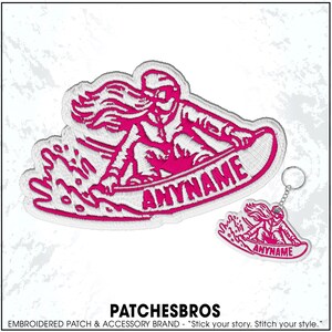 May include: Embroidered patch and keychain set featuring a pink and white design of a person snowboarding. The patch and keychain have the word "ANYNAME" on the snowboard. The brand name "PATCHESBROS" is at the bottom.