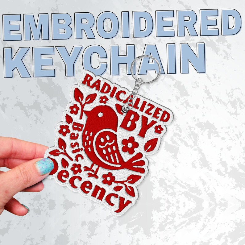 May include: Embroidered keychain with a red bird design and the words "RADICALIZED BY BASIC decency." The keychain has a silver metal ring. The background is a light gray with the words "EMBROIDERED KEYCHAIN" in blue.