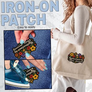 May include: An iron-on patch featuring a floral design with red, yellow, and purple flowers and green leaves. The text "radicalized by basic decency" is embroidered in white. The patch is shown being applied to blue denim and a beige tote bag.